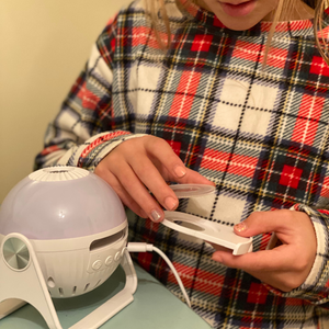 A close-up indoor daytime picture of the GloriLight, the globe nightlight projector. A child in pajamas is loaading a disc into the projector pull out with her hands.