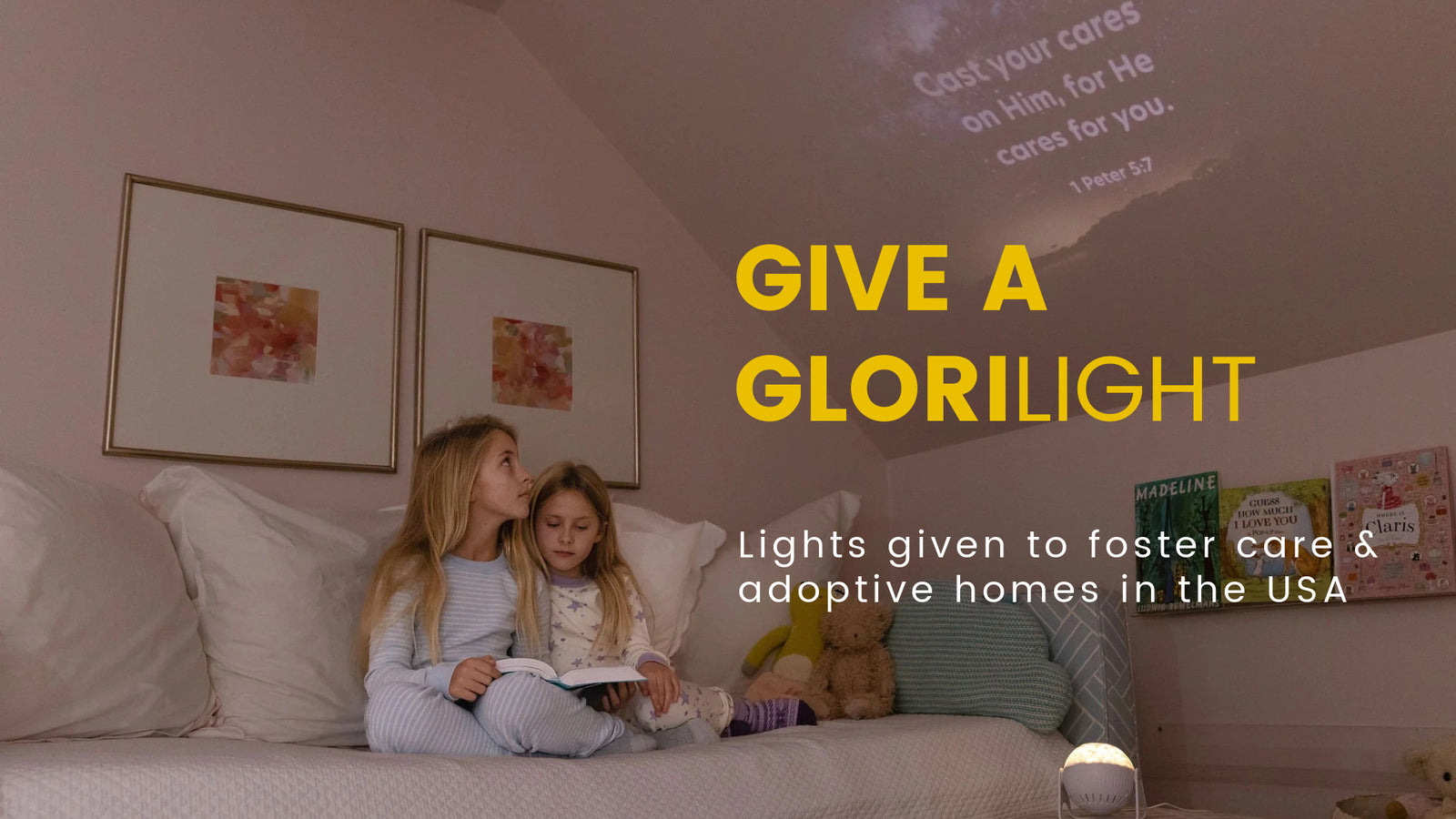 image of two young girls ages 11 and 7 sitting on a bed looking up at the ceiling. The glorilight is turned on and displays the image in the ceiling with the Bible verse 1 Peter 5:7.  Cast your cares on Him, for He cares for you.  Text overlayed on the image reads: Give a GloriLight.  Lights given to foster care and adoptive homes in the USA. 