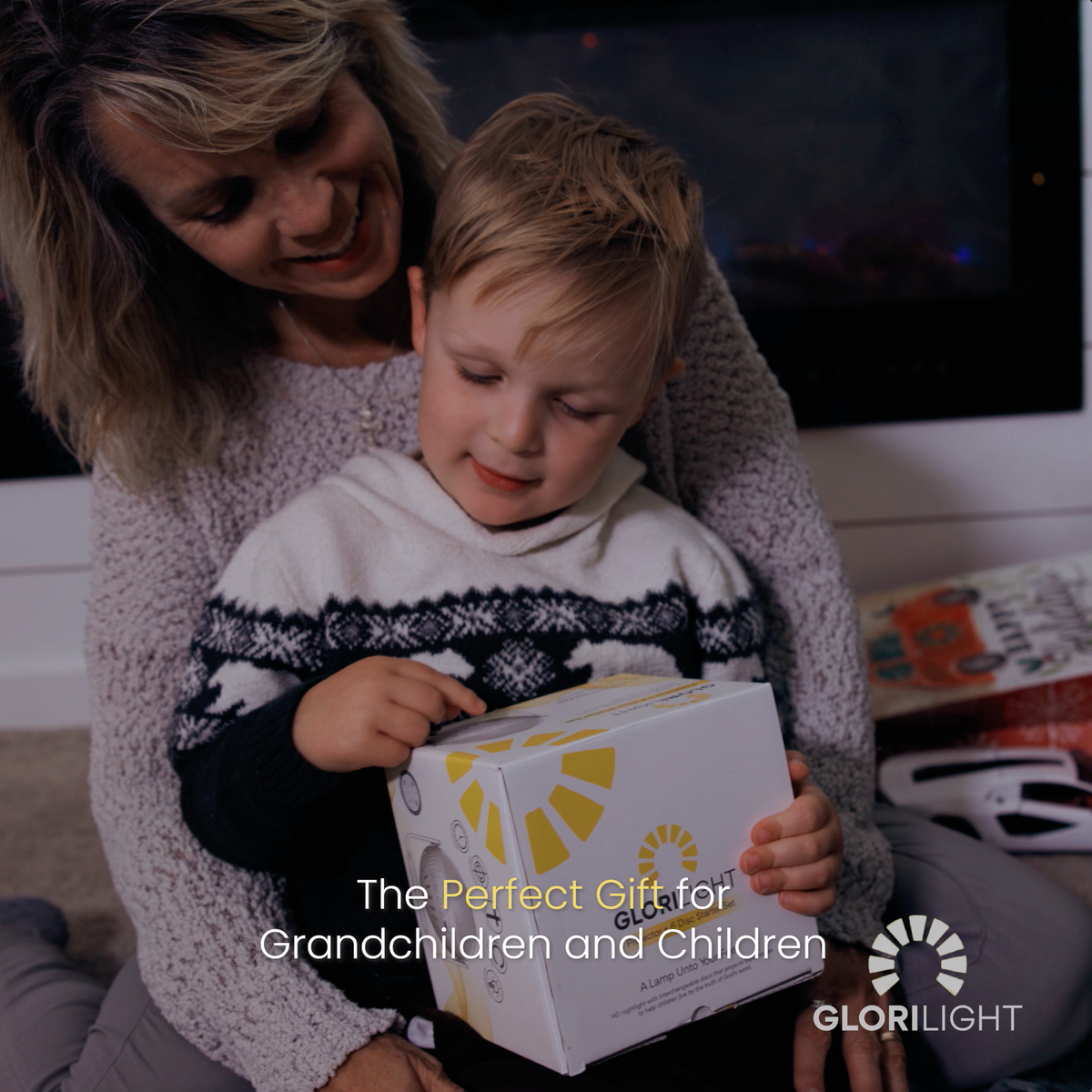  Picture of mom holding small child in her lap holding the GloriLight box. Text at the bottom center reads, the perfect gift for grandchildren and children. GloriLight logo and name in the bottom right corner in white.