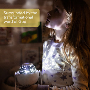 Eight year old girl in star pajama shirt looking toward ceiling as she holds the GloriLight shining all around. Text reads as Surounded by the transformational word of God.