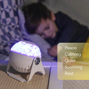 A slightly unfocused picture of a GloriLight lit up in the forefront on a nightstand in the left corner. In the right corner, text reads from top to bottom; peace, calming, quiet, soothing, rest. The text is encased in a yellow rectangle. In the background is a little boy sleeping on his bed.